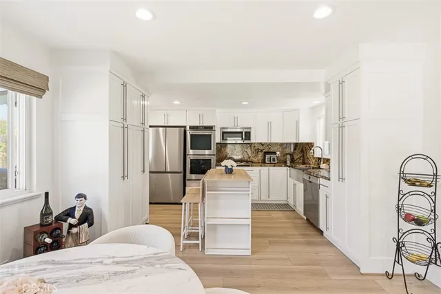 a kitchen with stainless steel appliances kitchen island granite countertop a refrigerator oven a stove top oven and white cabinets with wooden floor