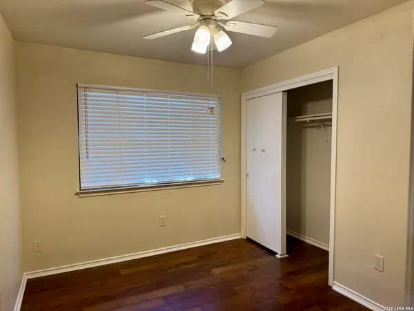 a view of an empty room with wooden floor and a chandelier fan