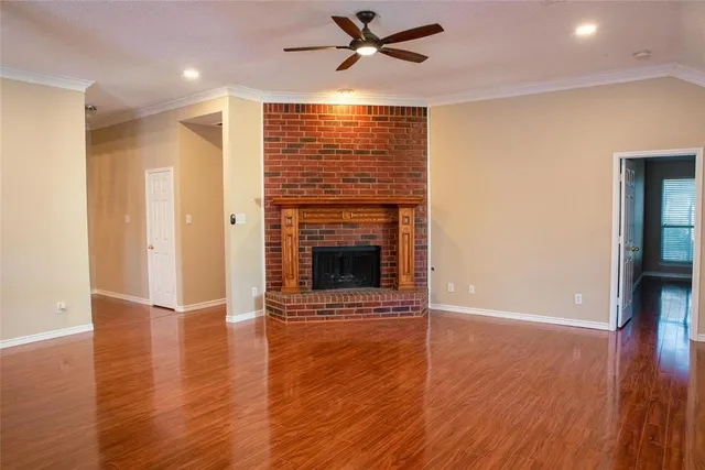 an empty room with wooden floor a ceiling fan a fireplace and windows