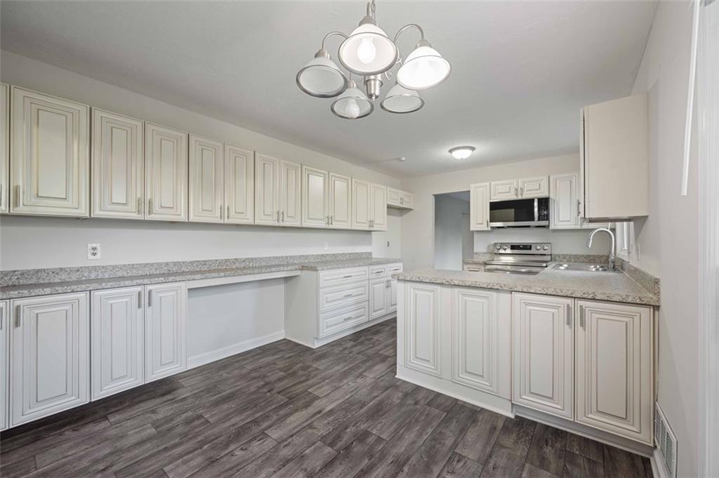 4166 Rue St Michel Stone Mountain, GA 30083 - Photo 17 of 31 a kitchen with stainless steel appliances granite countertop a sink dishwasher a stove top oven a refrigerator with white cabinets and wooden floor