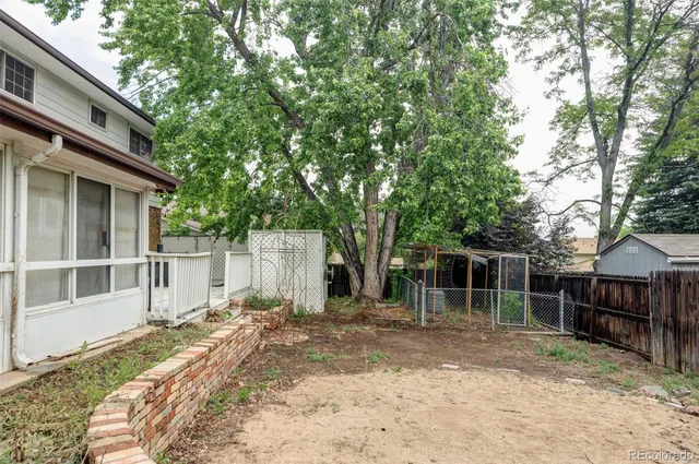 a backyard of a house with large trees and wooden fence