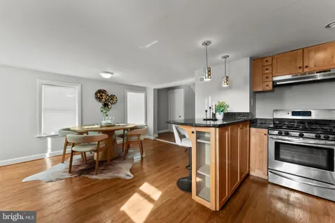 a kitchen with stainless steel appliances granite countertop a stove top oven a sink a dining table and chairs with wooden floor