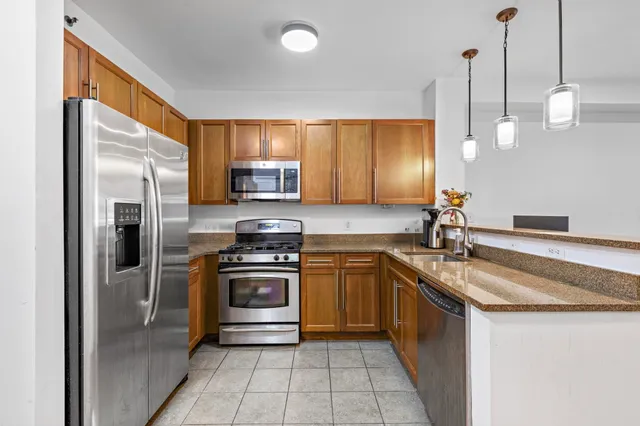 a kitchen with stainless steel appliances granite countertop a sink a stove a refrigerator a washer dryer and with wooden cabinets