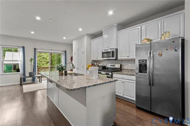 a kitchen with stainless steel appliances granite countertop a refrigerator a sink dishwasher a stove and white cabinets with wooden floor