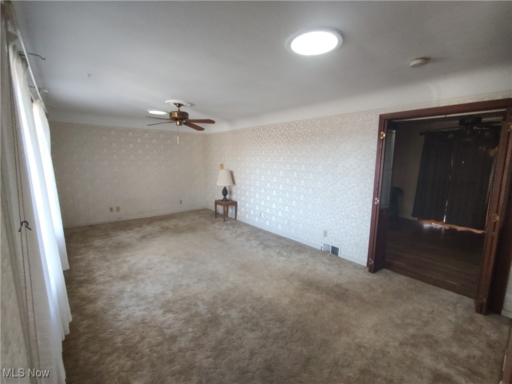 5704 Middle Ridge Road Madison, OH 44057 - Photo 12 of 50 Carpeted empty room featuring wallpapered walls, ceiling fan, and visible vents