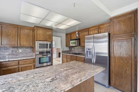 a kitchen with stainless steel appliances granite countertop a refrigerator a stove and a sink with wooden cabinets