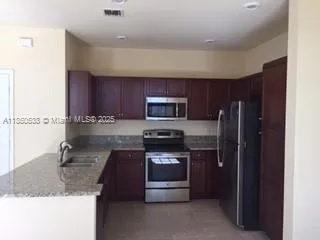 a kitchen with stainless steel appliances granite countertop a stove a refrigerator and a sink with wooden cabinets