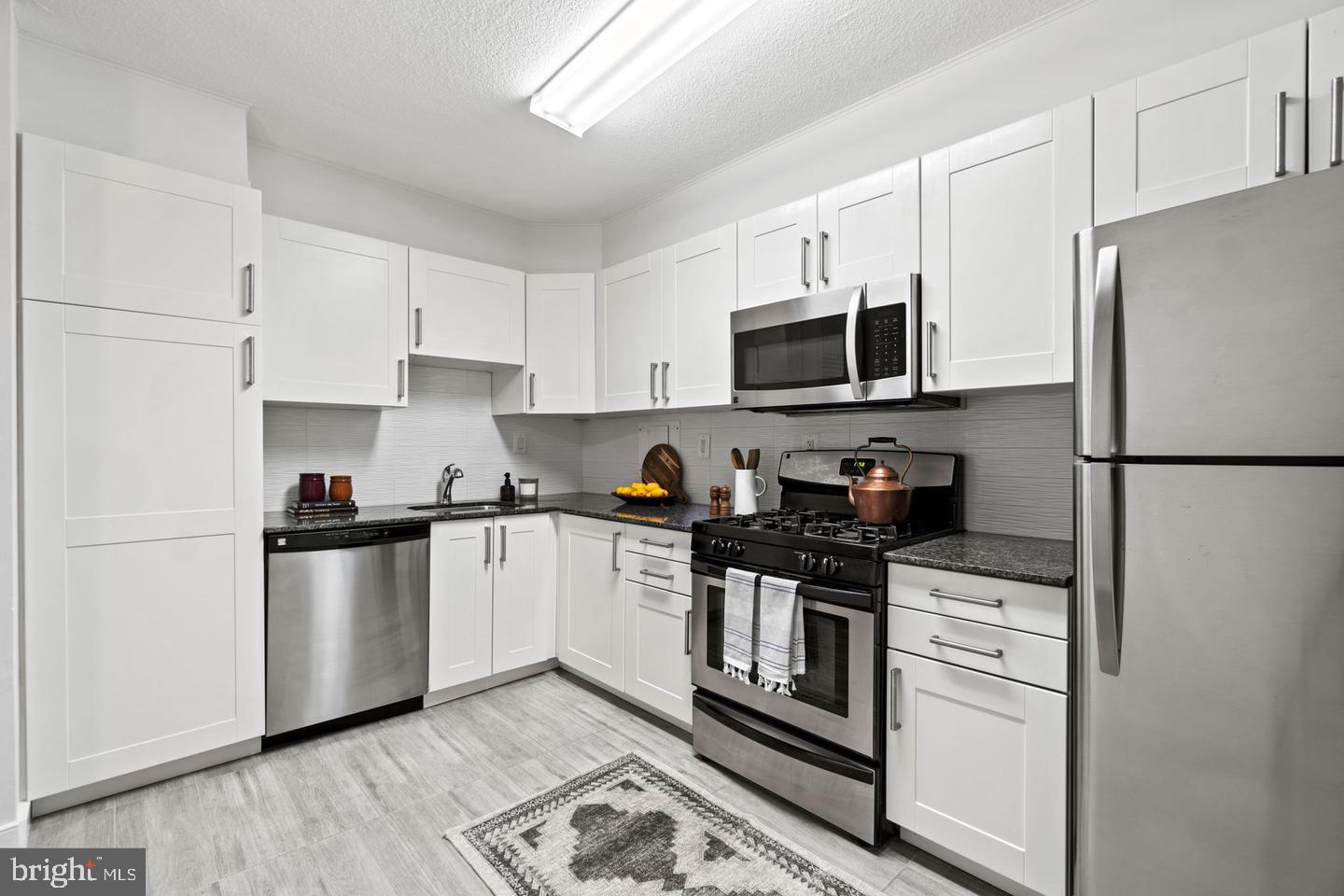 1300 Army Navy Drive, Unit 104 Arlington, VA 22202 - Photo 5 of 19 a kitchen with stainless steel appliances granite countertop a refrigerator stove a sink and a microwave