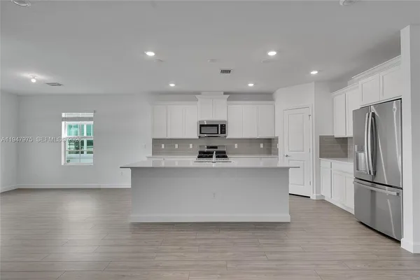 a large white kitchen with wooden floor a sink and a refrigerator
