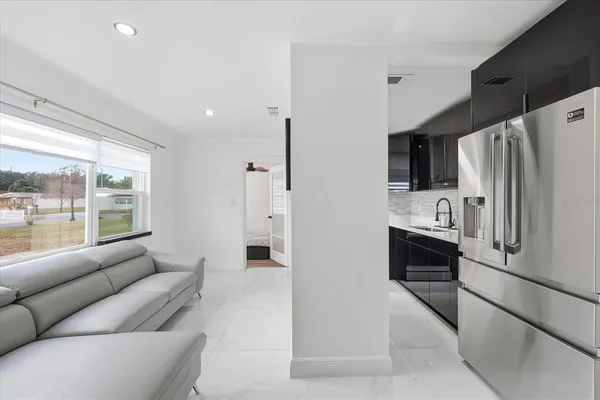 a living room with stainless steel appliances furniture windows and a kitchen view