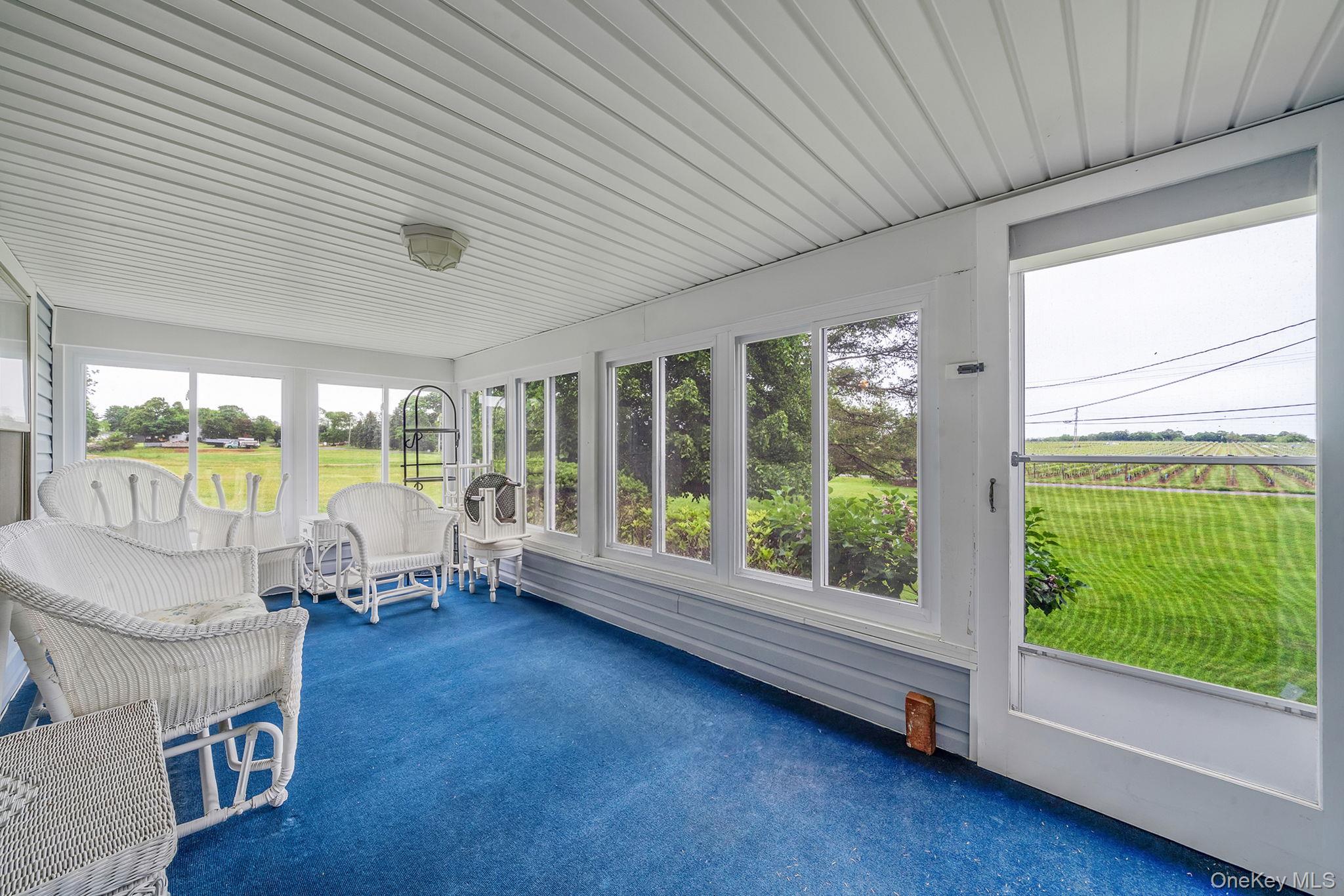 1055 Oregon Road Mattituck, NY 11952 - Photo 26 of 33 Enclosed porch with a scenic view. Featuring a carpeted floor, white paneled ceiling, multiple Andersen windows, and a screen door. Access from the Parlor.