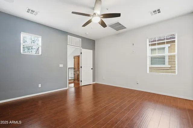 an empty room with wooden floor chandelier fan and windows