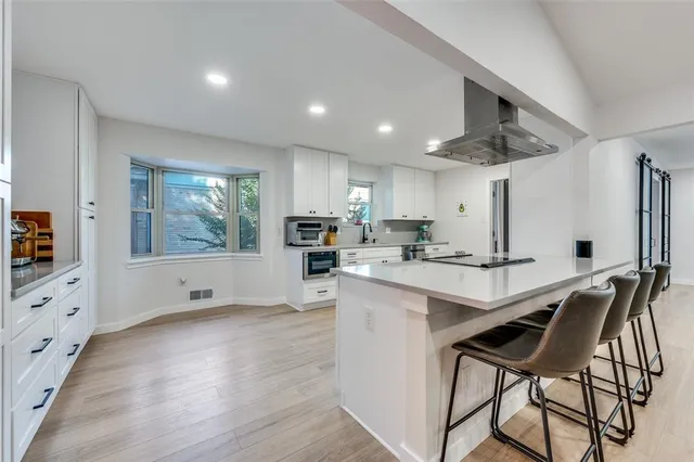 a kitchen with stainless steel appliances kitchen island granite countertop a stove a sink a refrigerator and white cabinets with wooden floor