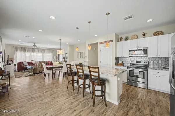 a large kitchen with white cabinets a stove a dining table and chairs with wooden floor