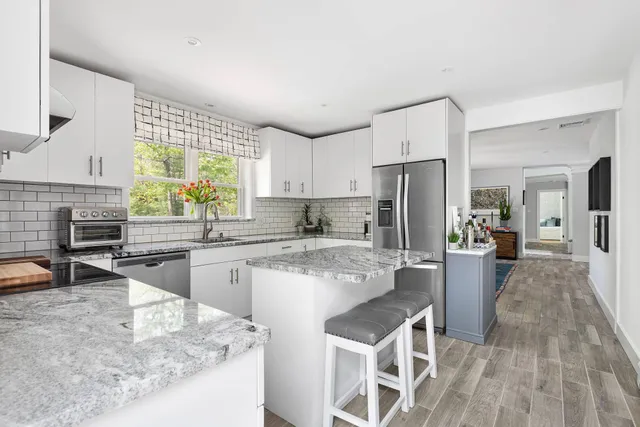 a kitchen with stainless steel appliances granite countertop a refrigerator a sink dishwasher a stove and white cabinets with wooden floor