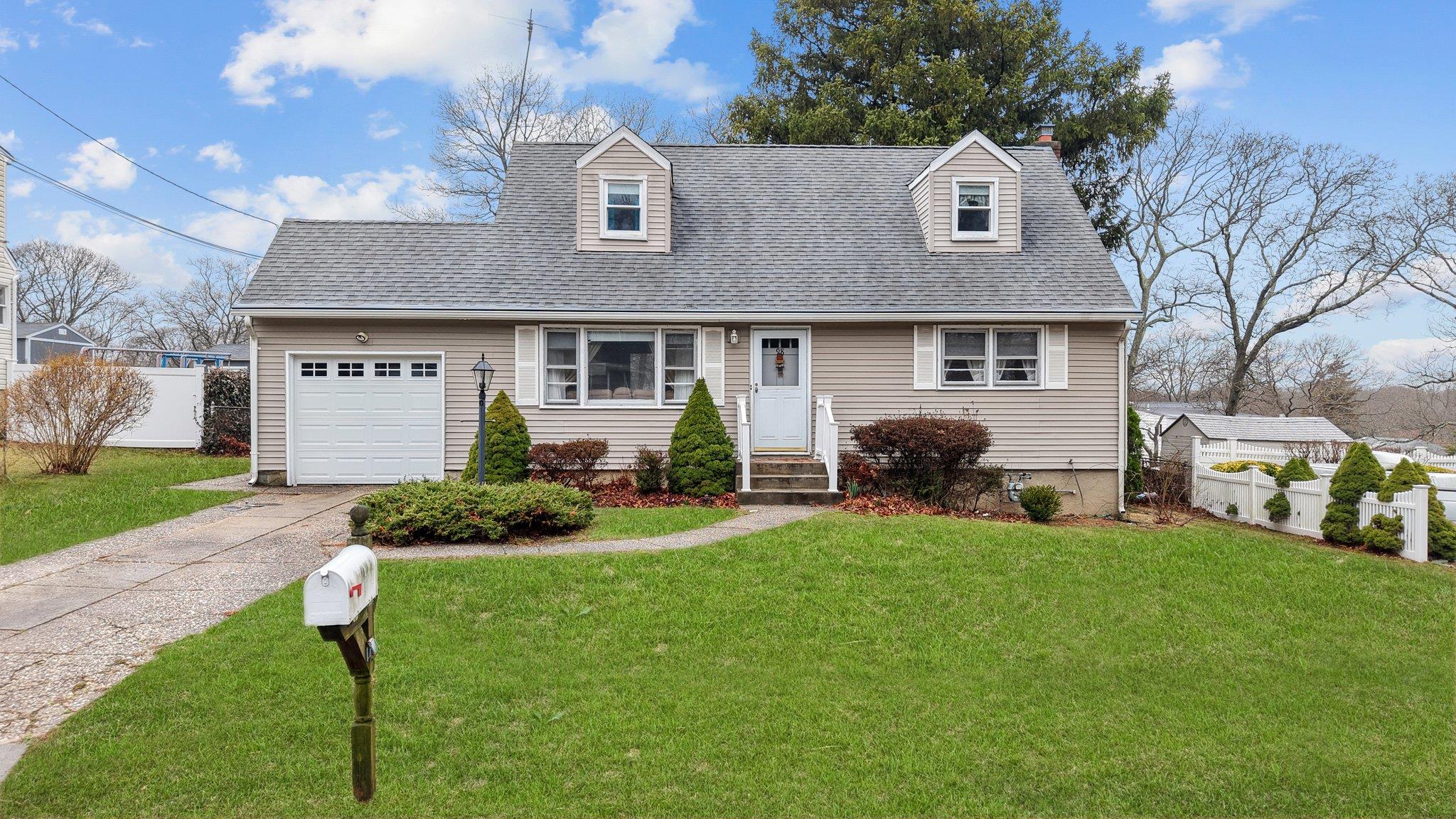Cape cod home with a shingled roof, fence, concrete driveway, a front yard, and a garage