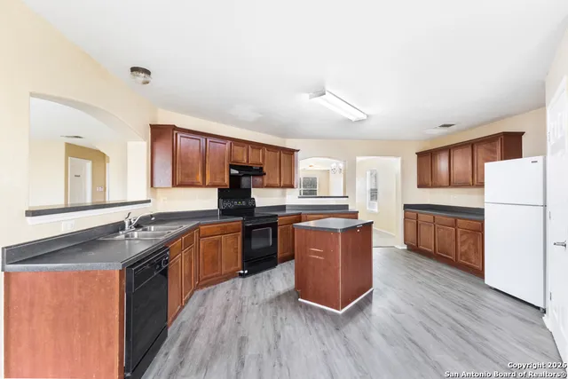 a large kitchen with stainless steel appliances granite countertop a stove a sink dishwasher a refrigerator and white cabinets with wooden floor