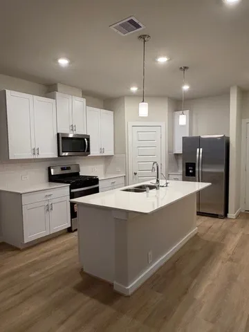 a large kitchen with stainless steel appliances kitchen island granite countertop a large stove a sink a refrigerator and white cabinets with wooden floor