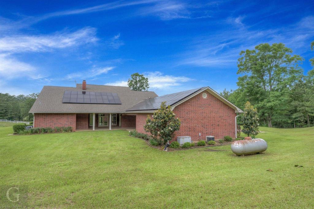 1212 WPA Road Homer, LA 71040 - Photo 7 of 35 Rear view of house with brick siding, a lawn, roof mounted solar panels, cooling unit, and a chimney