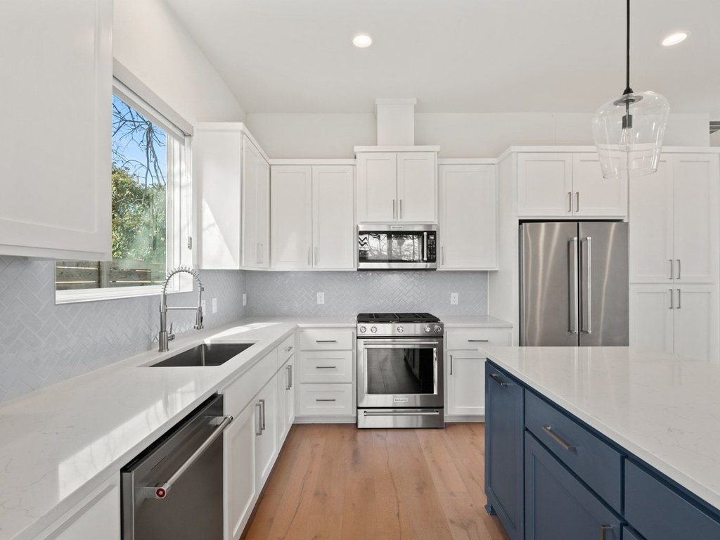 709 West St Elmo Road, Unit 2 Austin, TX 78745 - Photo 10 of 26 Dual tone kitchen with stainless steel appliances, light stone countertops, light wood-style floors, decorative light fixtures, and dual tone cabinetry