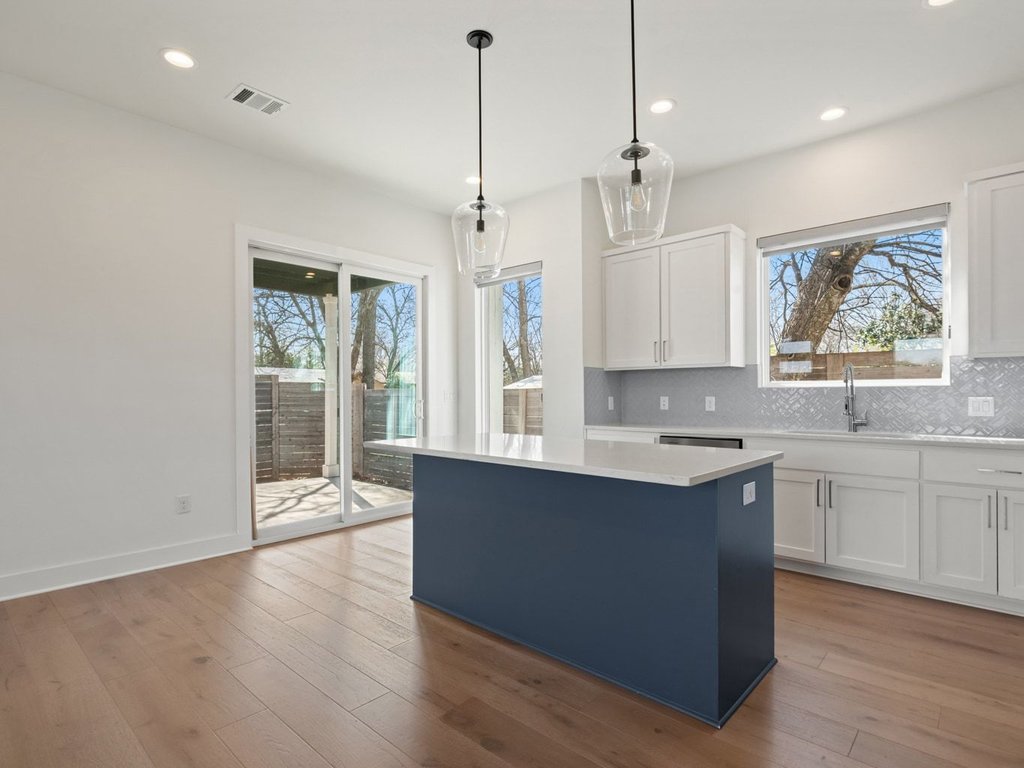 709 West St Elmo Road, Unit 2 Austin, TX 78745 - Photo 3 of 26 Dual tone kitchen with two tone cabinetry, pendant lighting, light wood finished floors, backsplash, and a center island