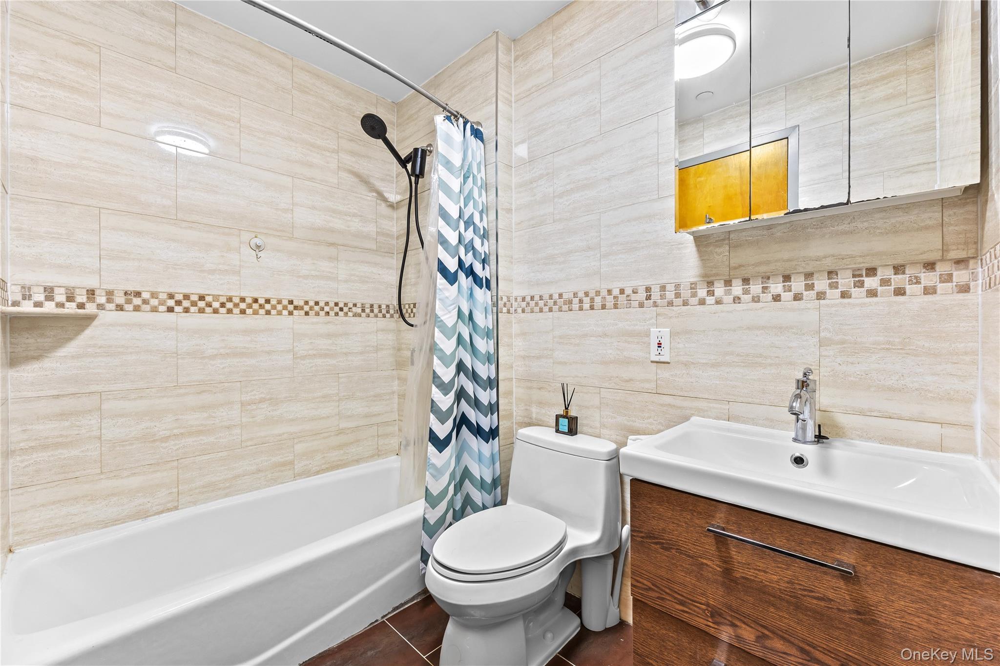 95-08 65th Road, Unit 3C Queens, NY 11374 - Photo 12 of 19 Full bath with tile walls, shower / bath combo with shower curtain, vanity, and dark tile patterned flooring