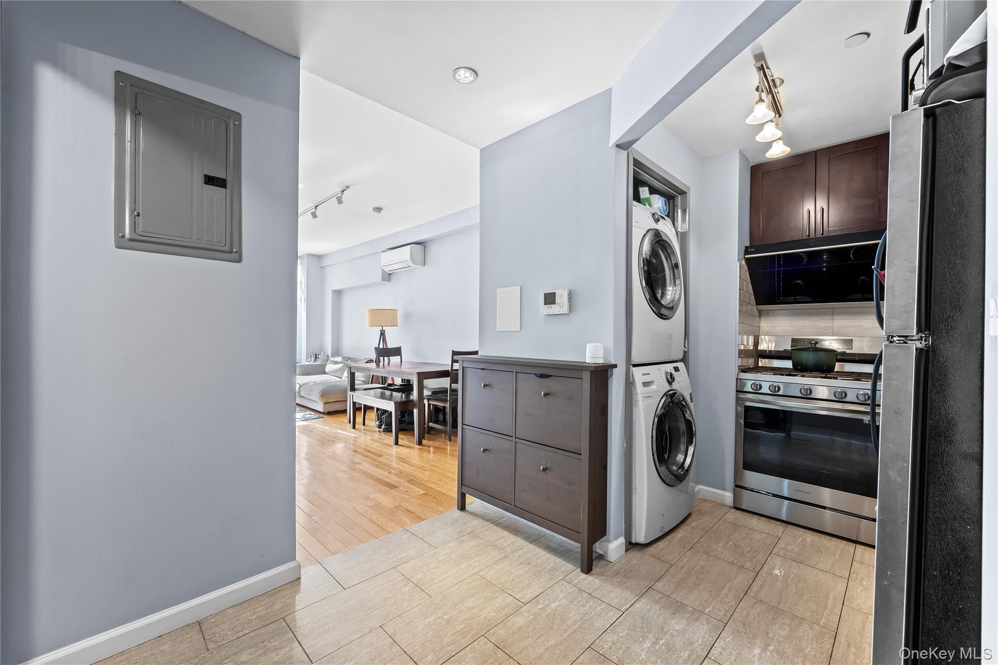 95-08 65th Road, Unit 3C Queens, NY 11374 - Photo 6 of 19 Kitchen featuring track lighting, appliances with stainless steel finishes, stacked washer / dryer, electric panel, and dark brown cabinets