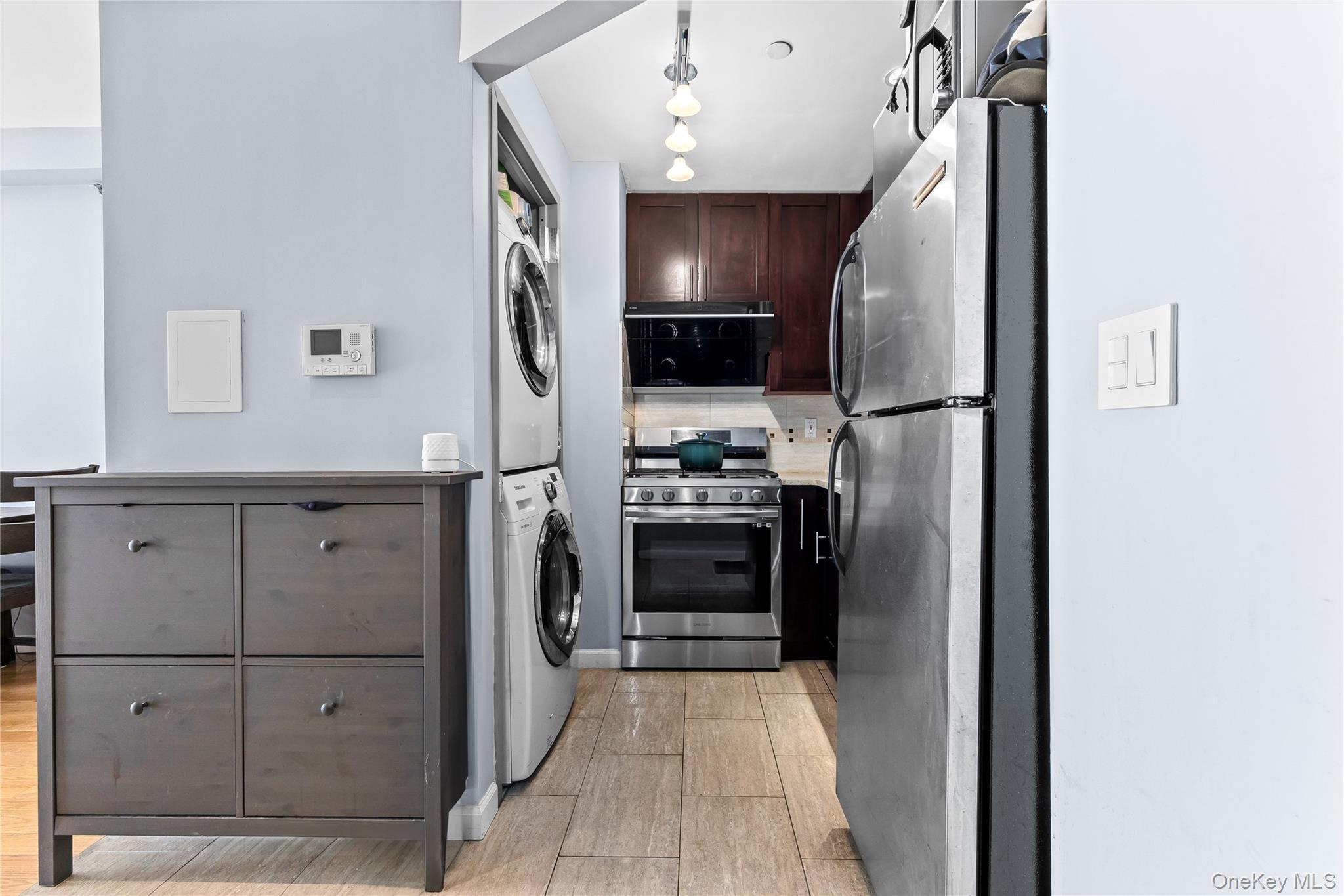 95-08 65th Road, Unit 3C Queens, NY 11374 - Photo 7 of 19 Kitchen with stainless steel appliances, stacked washer / dryer, tasteful backsplash, light countertops, and dark brown cabinets