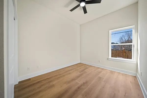 an empty room with wooden floor fan and windows