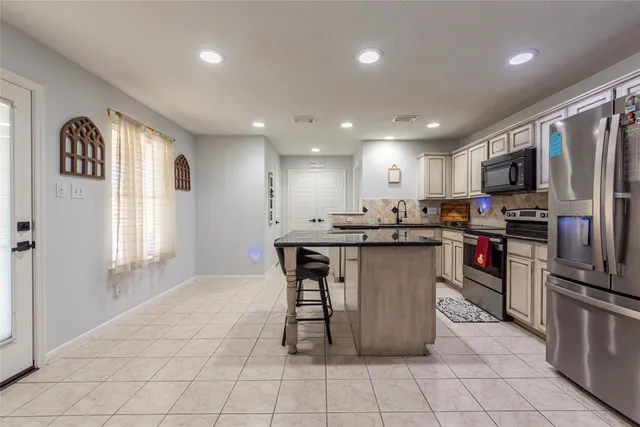 a kitchen with stainless steel appliances granite countertop a refrigerator a sink a stove a microwave and a dining table with wooden cabinet