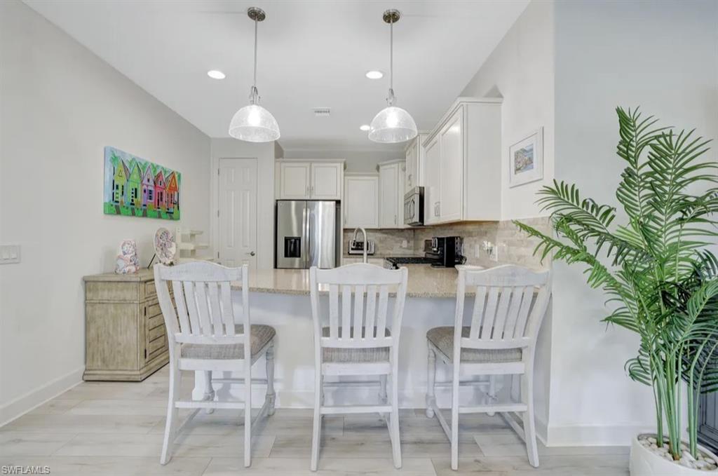 20183 Torch Key Way Estero, FL 33928 - Photo 5 of 30 Kitchen featuring a peninsula, stainless steel appliances, white cabinetry, light stone countertops, and hanging light fixtures