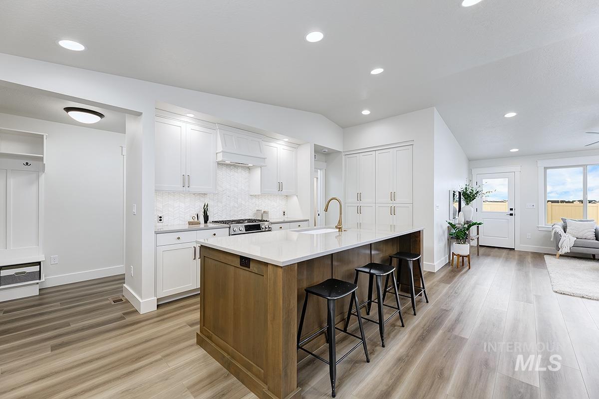 6975 South Skybreak Lane Meridian, ID 83642 - Photo 3 of 29 Kitchen with two tone cabinetry, a kitchen bar, an island with sink, light wood-style floors, and backsplash