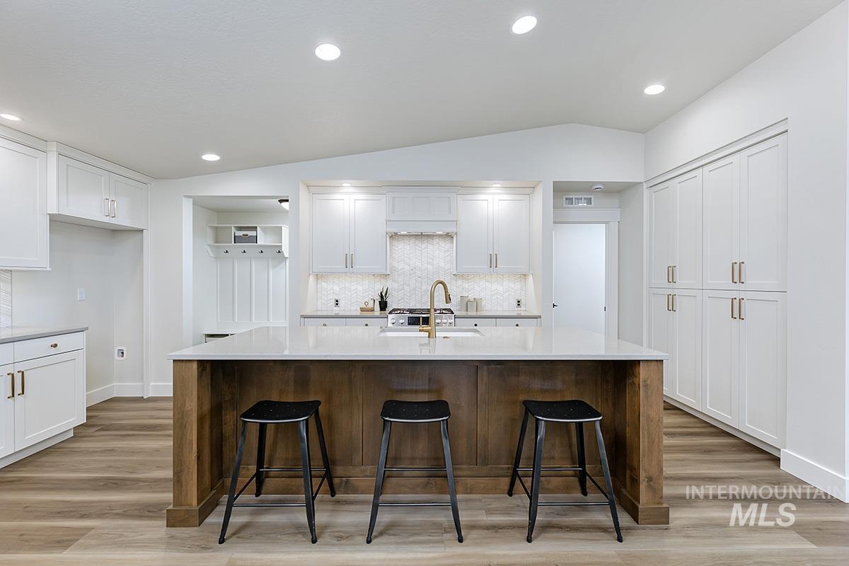 6975 South Skybreak Lane Meridian, ID 83642 - Photo 4 of 29 Kitchen with lofted ceiling, a kitchen island with sink, light wood-style flooring, decorative backsplash, and two tone cabinets