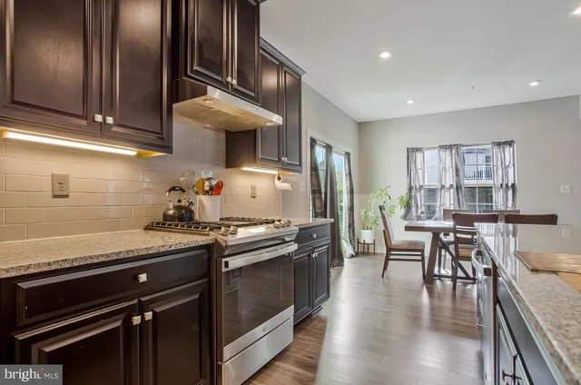 a kitchen with stainless steel appliances granite countertop a stove a refrigerator a microwave oven with white cabinets and wooden floor