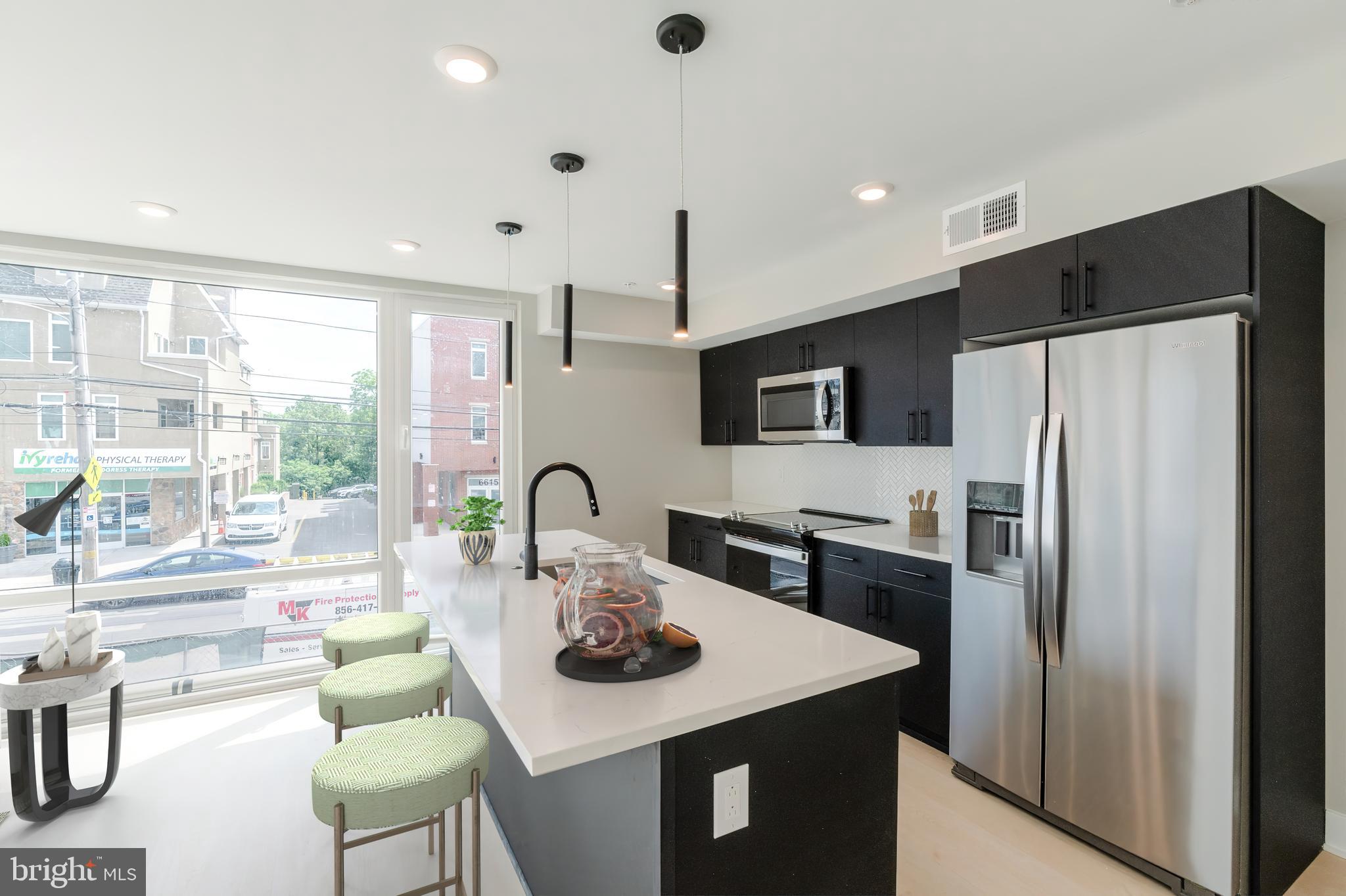 6604 Ridge Avenue, Unit 305 Philadelphia, PA 19128 - Photo 2 of 17 a kitchen with a refrigerator a stove a sink and a dining table with wooden floor