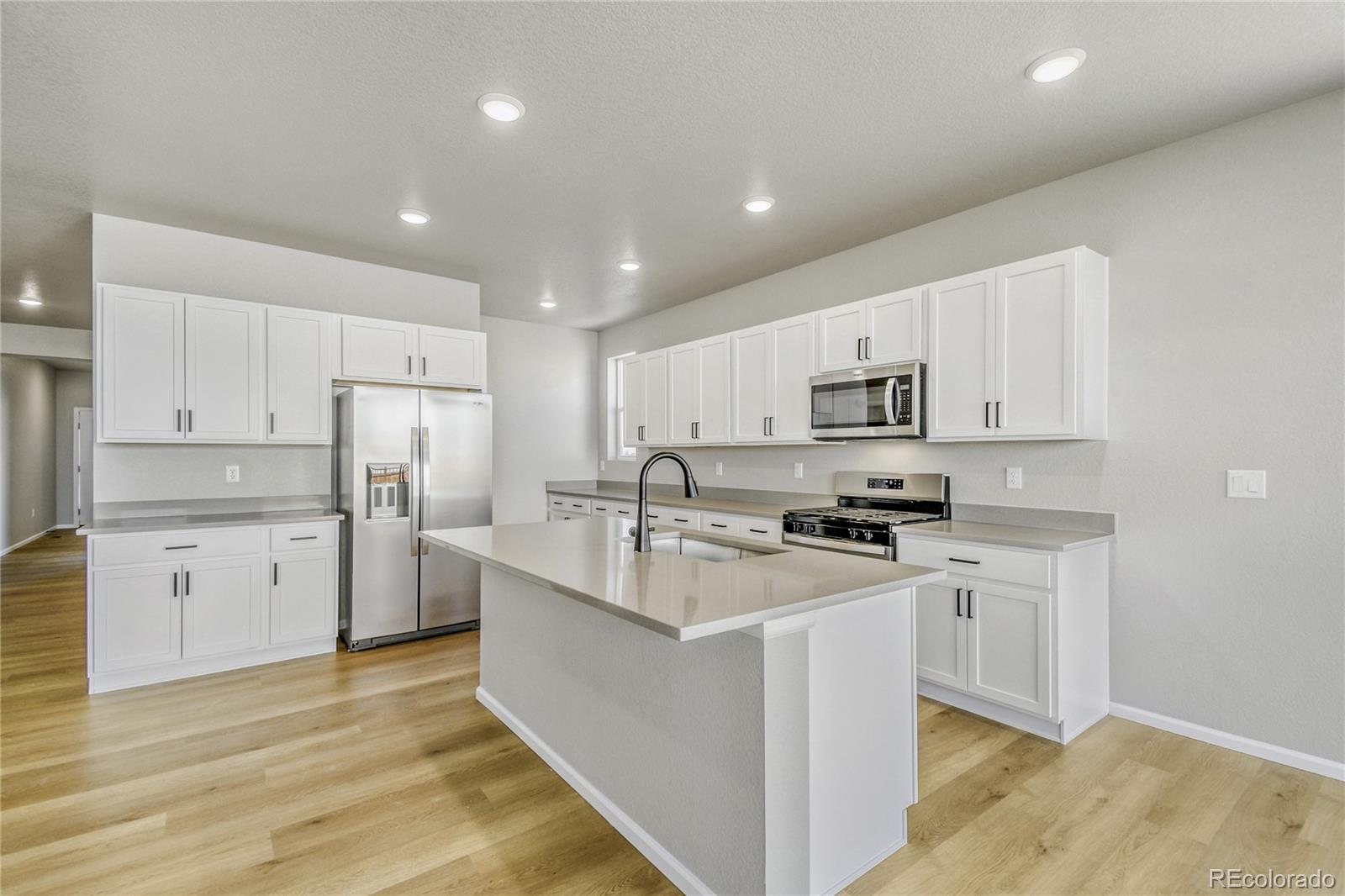 4135 Runyon Street Brighton, CO 80601 - Photo 6 of 27 a kitchen with refrigerator a stove a sink and white cabinets