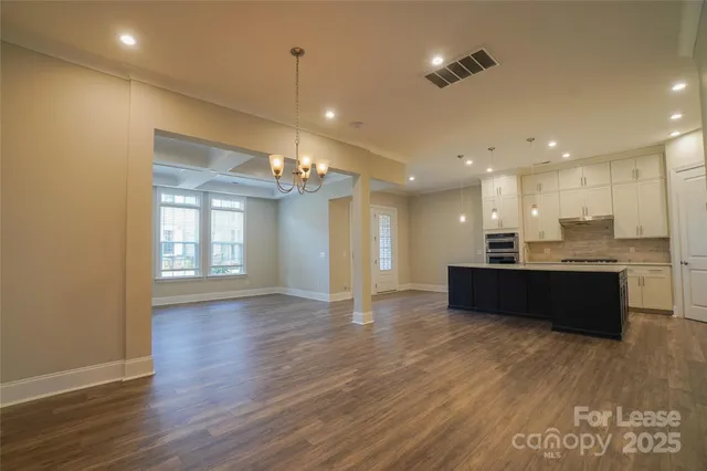 a view of an empty room and kitchen with wooden floor