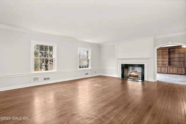an empty room with wooden floor fireplace and windows