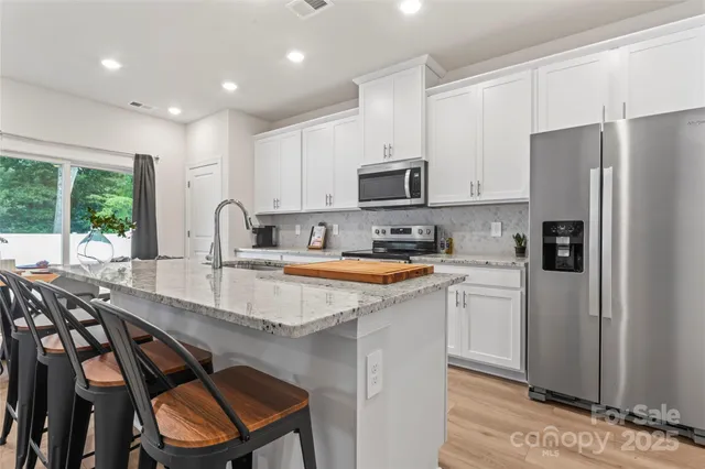 a kitchen with stainless steel appliances granite countertop a stove a sink a microwave a refrigerator and white cabinets with wooden floor