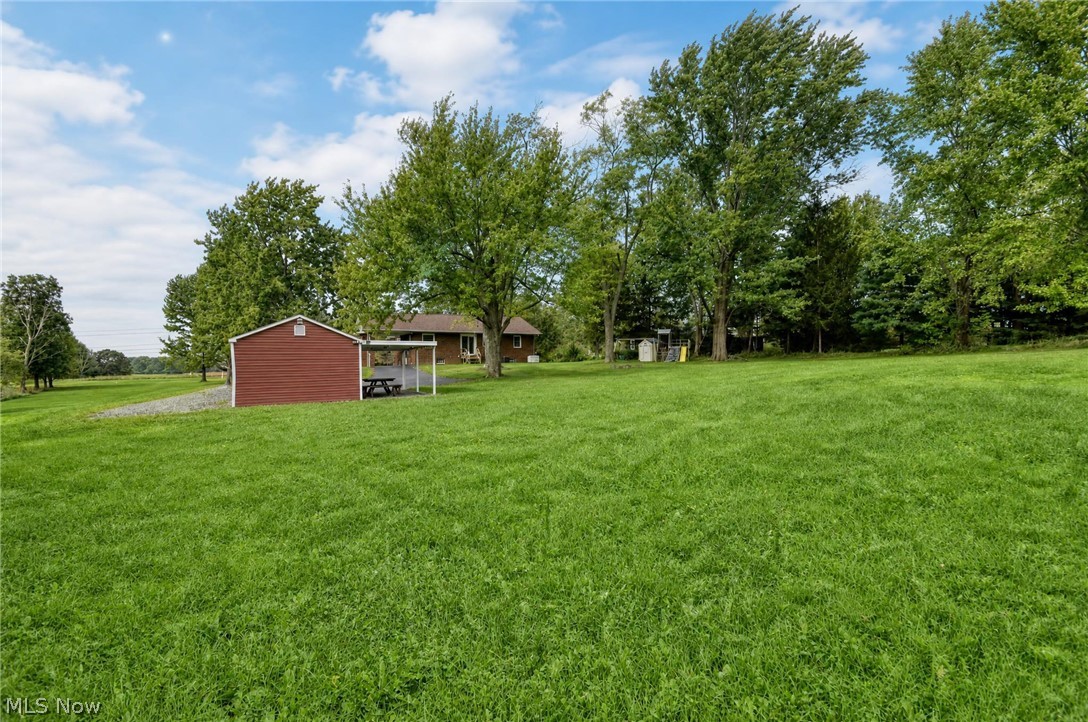 3864 State Road South Ashtabula, OH 44004 - Photo 49 of 50 Expansive green lawn with mature trees and a red storage shed featuring an attached carport