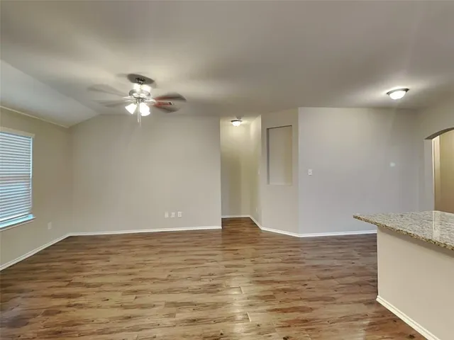 a view of an empty room with wooden floor and a ceiling fan