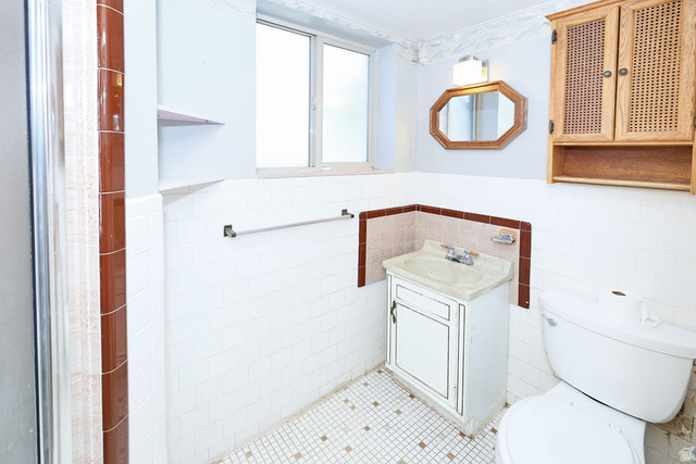 1272 Cook Street Ogden, UT 84404 - Photo 20 of 46 Bathroom featuring white wall tile with brown accent trim, a window with frosted glass, a wall-mounted octagonal mirror, a vanity with a drop-in sink, and a commode