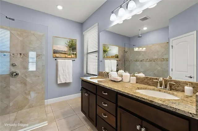 a bathroom with a granite countertop double vanity sink a mirror and a shower