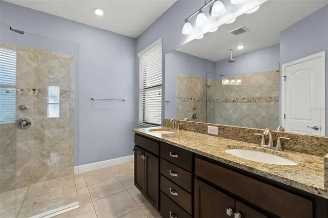 a bathroom with a granite countertop double vanity sink a mirror and a shower