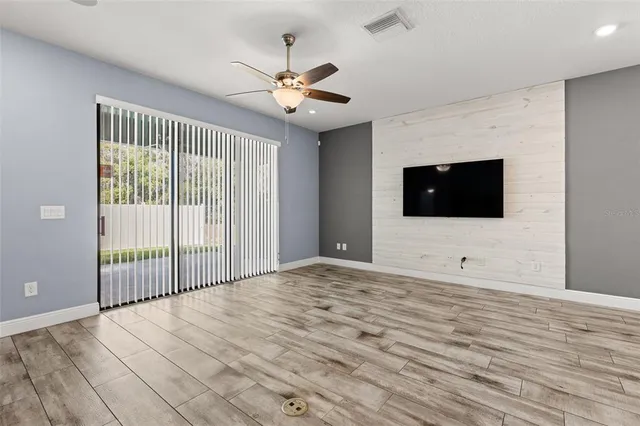 a view of an empty room with wooden floor and fan
