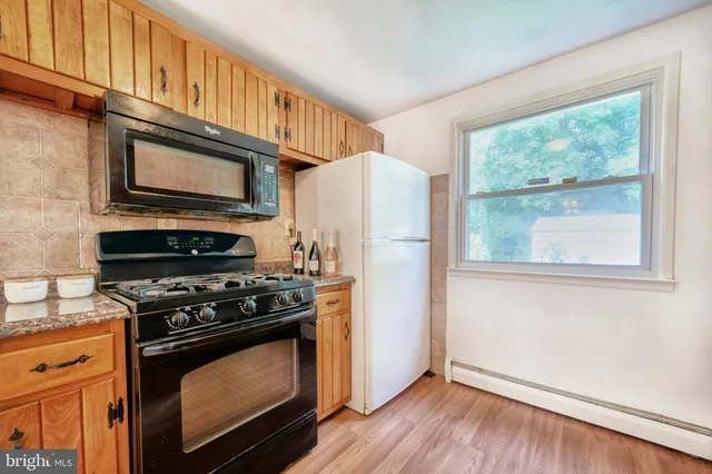 a kitchen with granite countertop wooden cabinets a stove a refrigerator and wooden floor