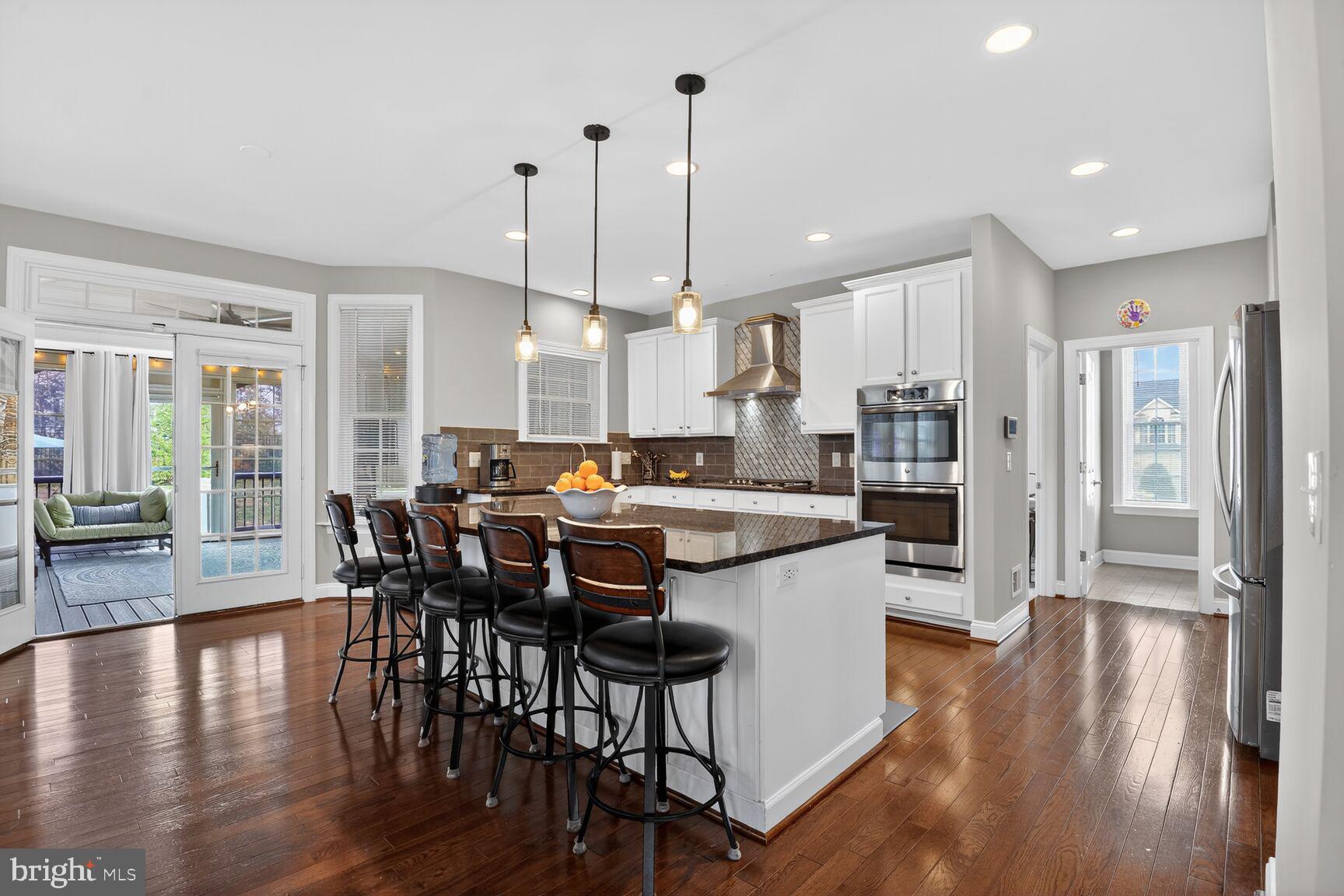 a kitchen with stainless steel appliances granite countertop a stove a refrigerator a kitchen island a dining table and chairs with wooden floor