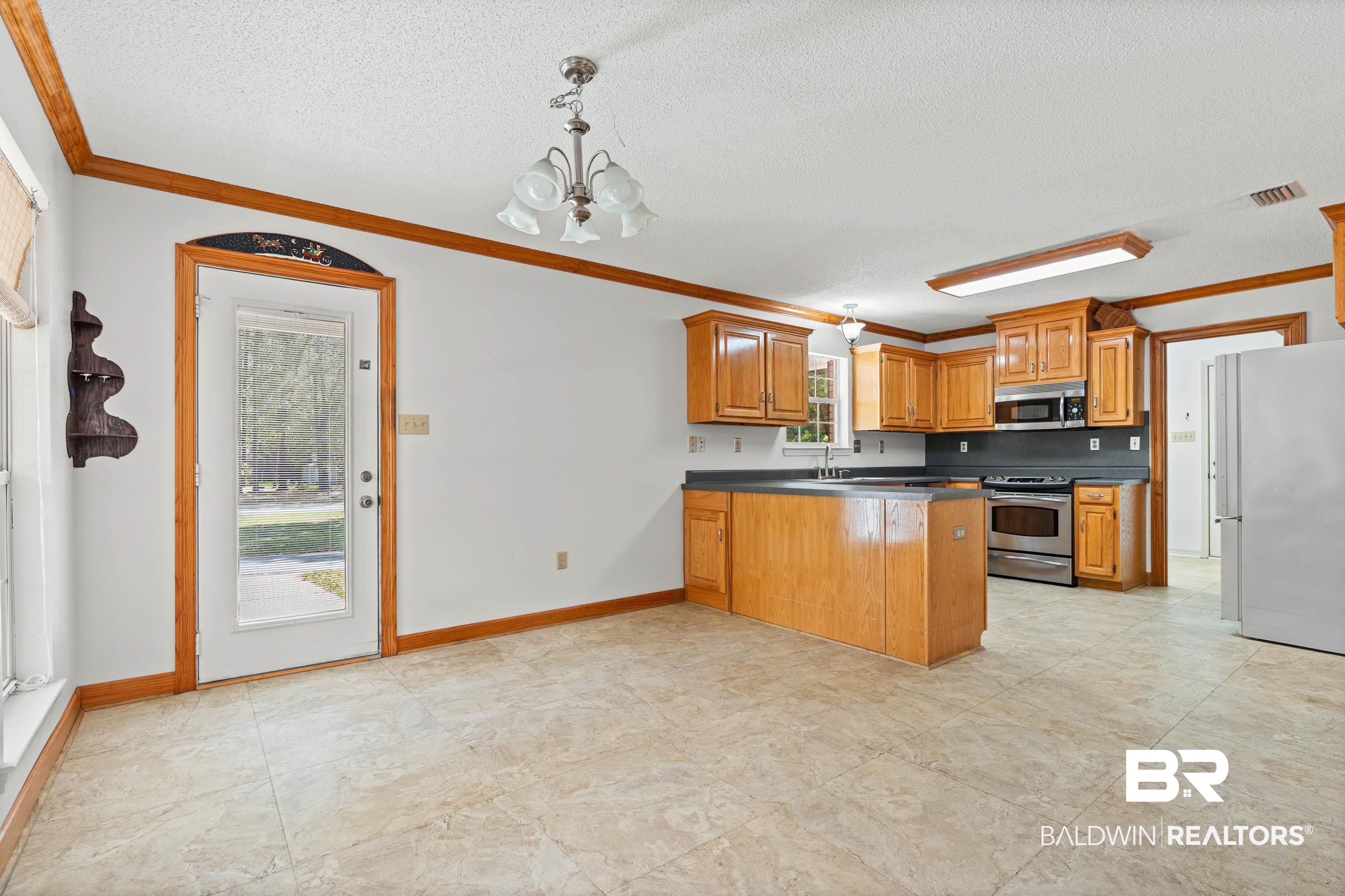 10140 Lakeview Road Bay Minette, AL 36507 - Photo 9 of 35 Kitchen with dark countertops, a peninsula, crown molding, stainless steel appliances, and wood finish cabinets
