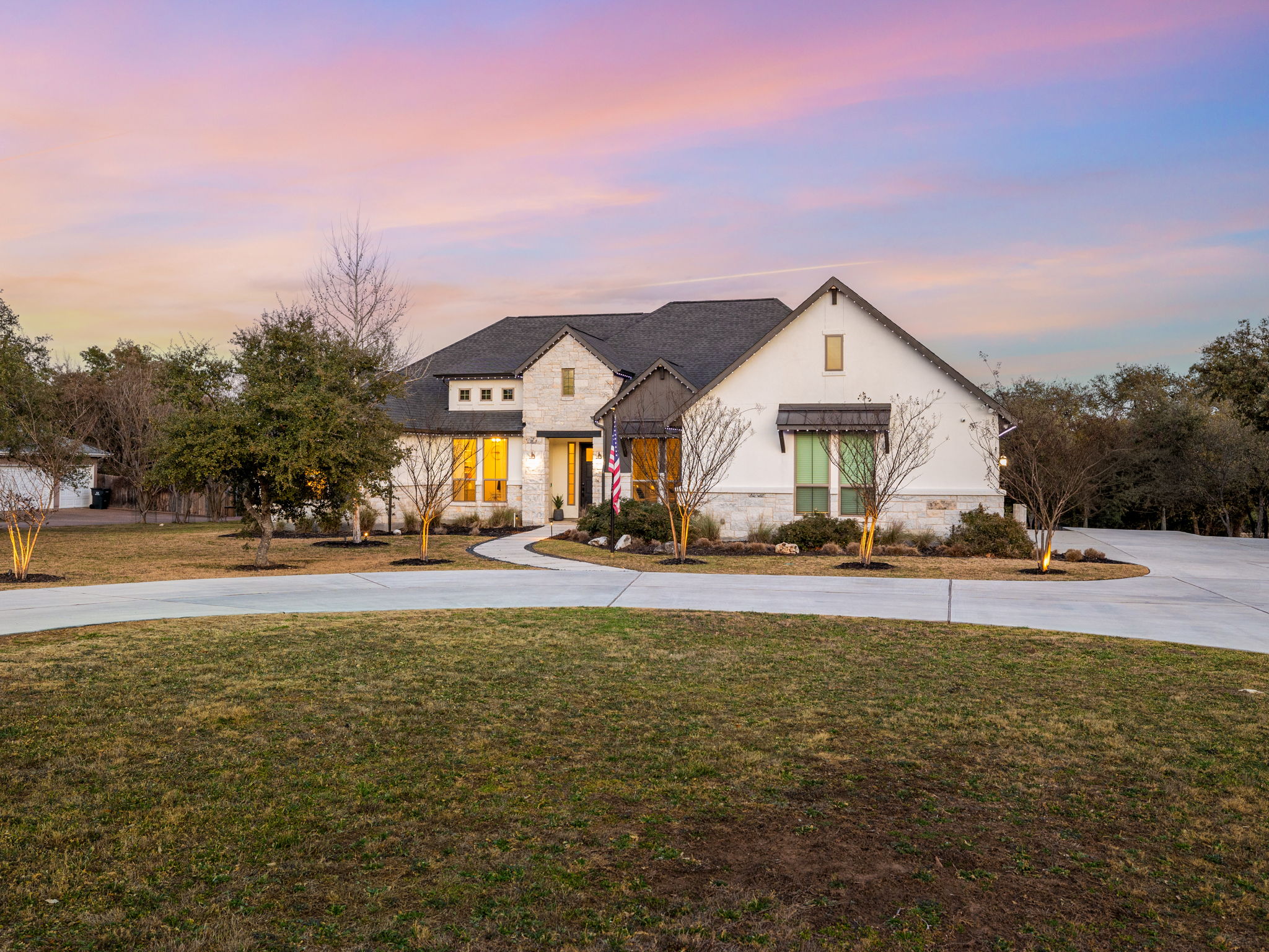 Modern farmhouse style home with stone siding, a front yard, and curved driveway