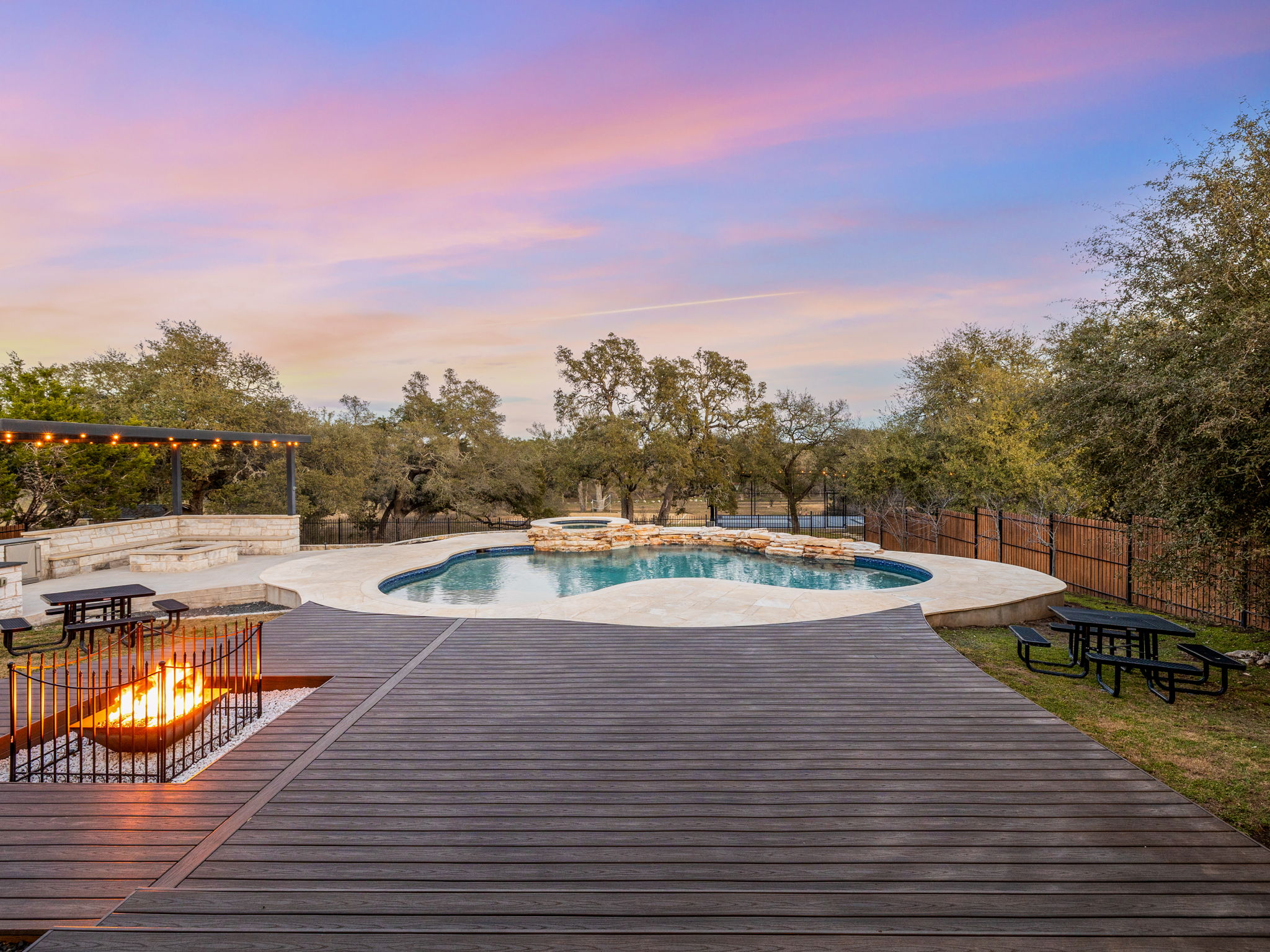 901 Clark Cove Road Buda, TX 78610 - Photo 32 of 37 Pool at dusk with a fire pit, a deck, a fenced backyard, a pool with connected hot tub, and a patio